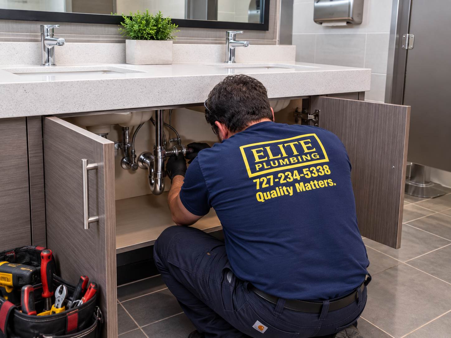 Elite Plumbing technician inspecting plumbing beneath sinks in a commercial restroom